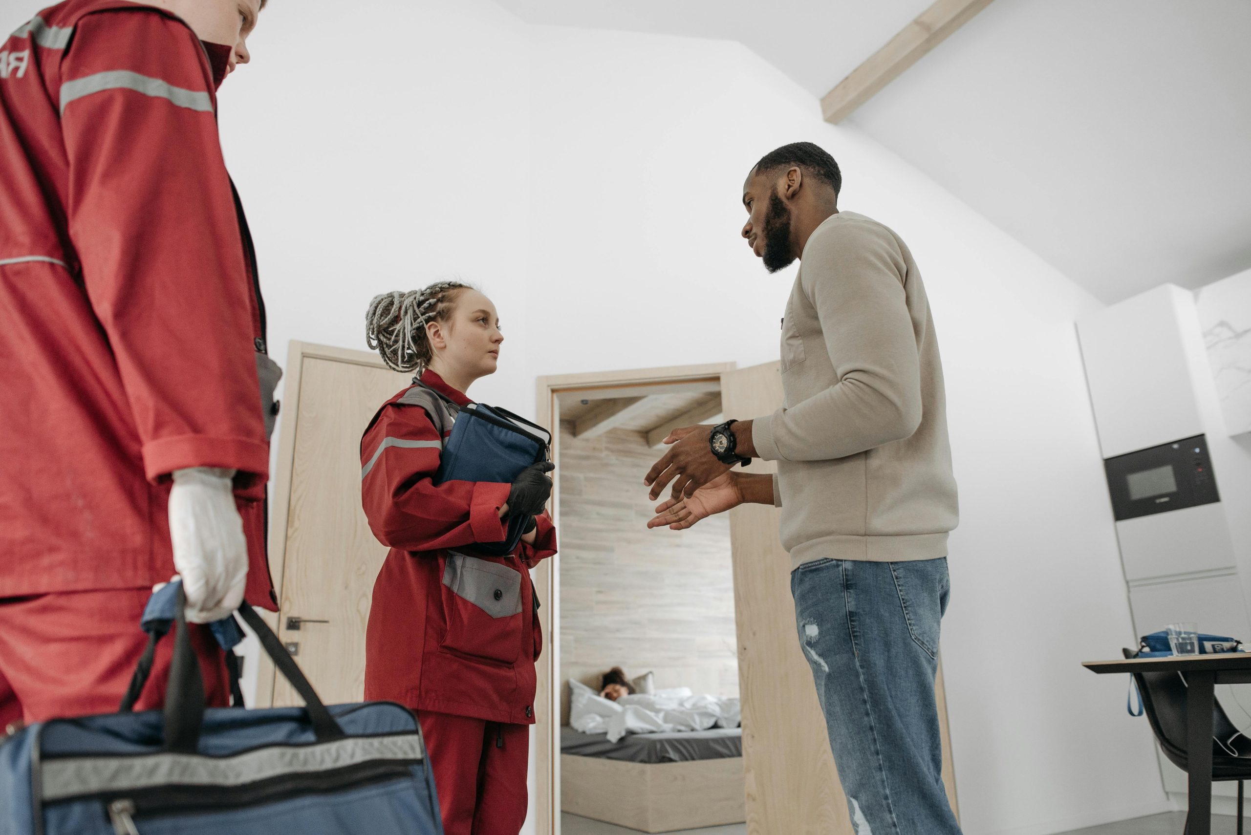 Paramedics in red uniforms assisting a person in a home setting, focusing on healthcare.