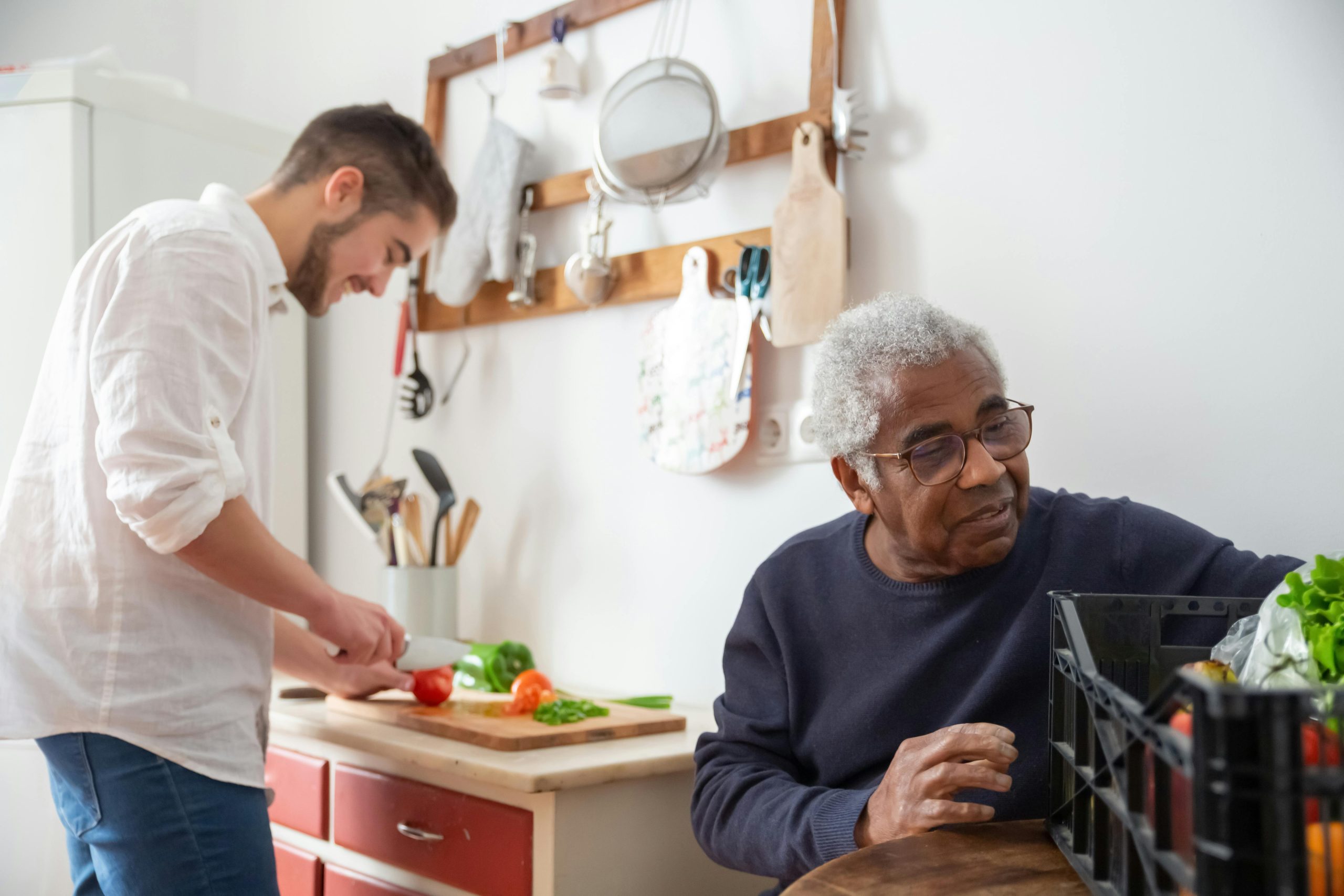 Services A senior man and young man preparing vegetables together in a cozy kitchen setting.